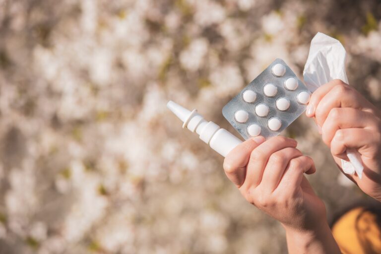 Nasenspray, Tabletten und ein Taschentuch vor einem blühenden Baum