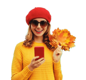 Frau mit Mütze und Herbstblättern schaut glücklich auf ihr Handy.