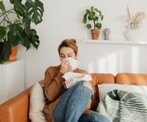 Eine Frau auf dem Sofa, die sich schnäuzt und Allergietabletten benötigt