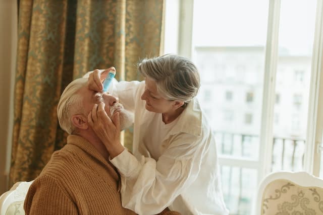 Eine Frau hilft einem Mann mit den Augentropfen gegen Allergie
