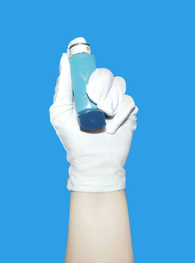 Eine Hand im Gummihandschuh mit einem Spray, das wie Salbutamol aussieht