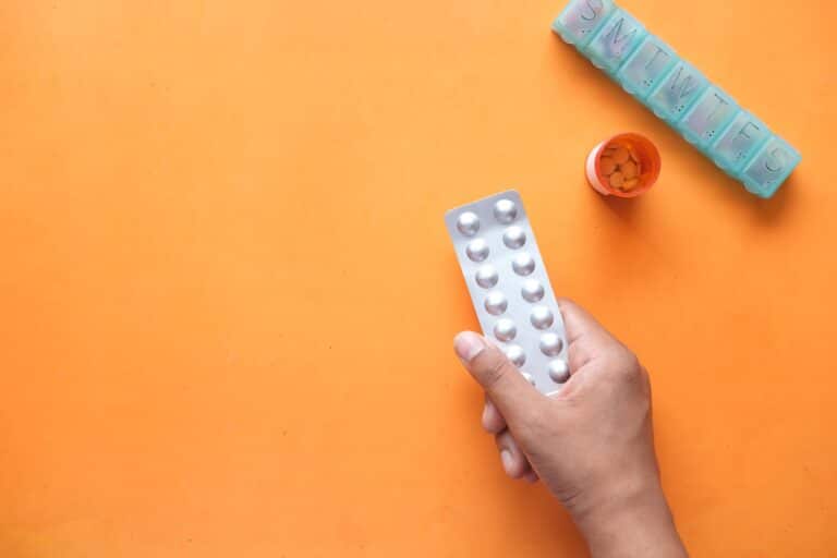 Hand mit Blisterpackung und Tabletten Dispenser. Die Tabletten sehen aus wie L-Thyrox