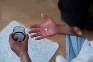 Mann mit einer Tablette Ritalin in der Hand und einem Wasserglas